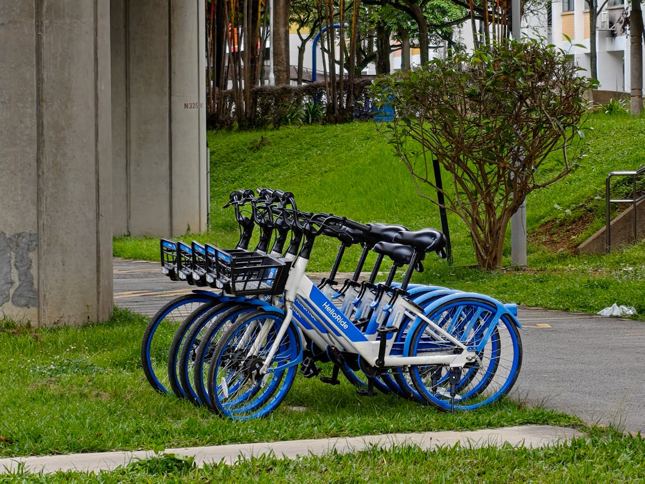 hero-img-01 A lineup of blue and white rental bikes parked outdoors beside a concrete structure.